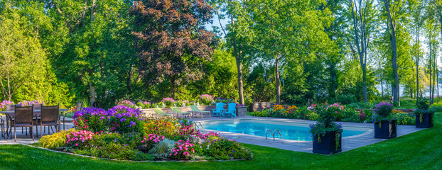 Residential swimming pool in a backyard with blossoming flowers and full trees; Hudson, Quebec, Canada