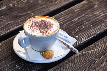 Cappuccino by an Italian cafe on wooden table, served with a small biscuit; Hexham, Northumberland, England