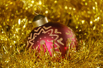 red christmas ball with golden pattern and new year tinsel on bokeh background