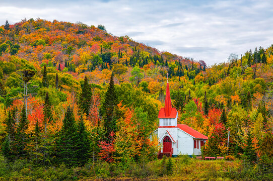 Country church in red and white hiding in the autumn coloured foliage in the hills; Sainte-Agathe-des-Monts, Quebec, Canada