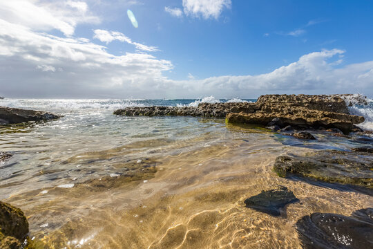 Serene, calm water on Hookipa Beach where surfers and sea turtles fill the beach and the rocks form scenic pools along the beach shore; Paia, Maui, Hawaii, United States of America