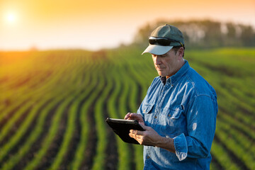 A farmer stands beside a farm field using a tablet; Alberta, Canada