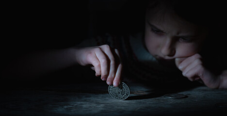 Sad young girl holding coins as symbol of poverty. Selective focus on yeys of girl. Horizontal...
