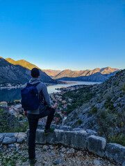 Man with panoramic view from the Ladder of Kotor on the Kotor bay during sunrise, Adriatic Mediterranean Sea, Montenegro, Balkan Peninsula, Europe. Winding fjord water reflection along coastal towns