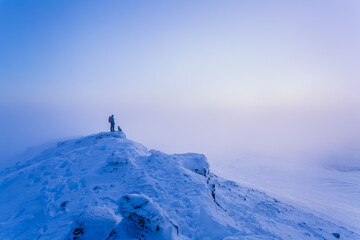 Man and dog hiking on top of snow-covered mountain in fog in the winter, Galty Mountains; County Tipperary, Ireland