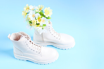 White demi-season martens boots with a bouquet of spring flowers on a light blue.
