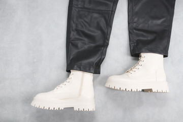White eco-leather ankle boots with buckles, laces and black stylish leather trousers on a gray cement