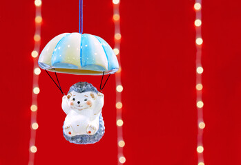 Ceramic figurine of a hedgehog flying on a parachute on a red background with a garland.