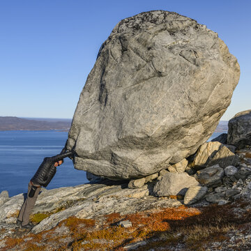 Man stands with hands on  a large boulder, giving the image of strength; Sermersooq, Greenland
