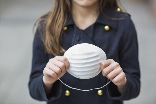 Young girl stands holding protective mask in her hands during the Coronavirus World Pandemic; Toronto, Ontario, Canada