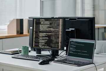 Workplace of developer with computer and laptop with codes on screens in modern office
