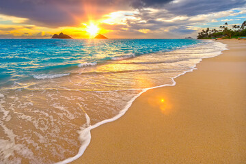 Lanakai Beach at sunrise, with the surf washing up on the golden sand and a view of the Mokulua Islands in the distance; Oahu, Hawaii, United States of America