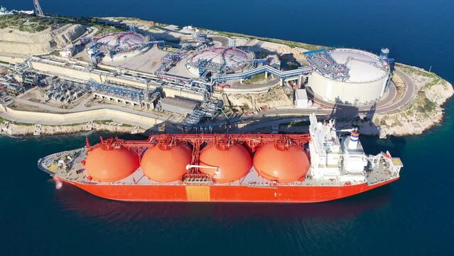 Aerial drone video of LNG (Liquified Natural Gas) tanker anchored in small LNG industrial islet of Revithoussa equipped with tanks for storage, Salamina, Greece