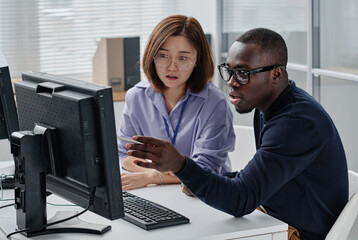 African American programmer pointing at monitor and discussing presentation with his colleague