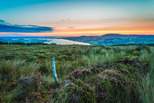 An old wooden fence post on a moor hill overlooking Lough Derg lake in the distance at sunrise; County Clare, Ireland