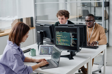 Group of young people sitting at their workplace and writing codes on computers, they working in IT office