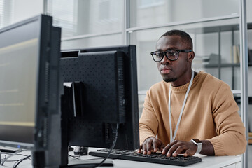 African American programmer in eyeglasses concentrating on his online work on computer, he typing...