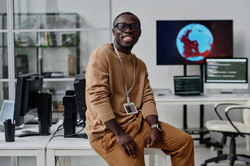 Portrait of young African American developer smiling at camera sitting on his workplace in IT office