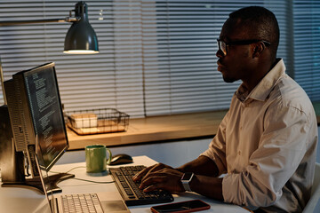 Serious African American programmer typing codes on keyboard for new computer program during work...