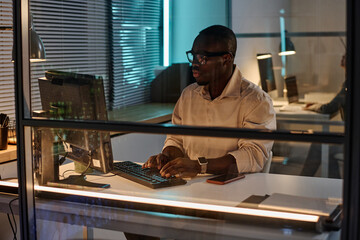African American businessman concentrating on his work on computer during his work in dark office