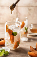 Making Apricot cocktail, fizz, ice tea with fresh mint and honey in process. Pink beige tile background