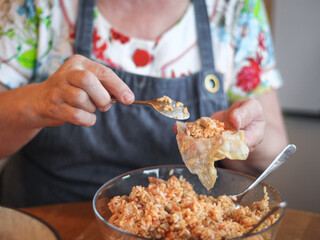 The hands of a senior woman hold a straightened leaf of sauerkraut in the palm and put a rice-meat
