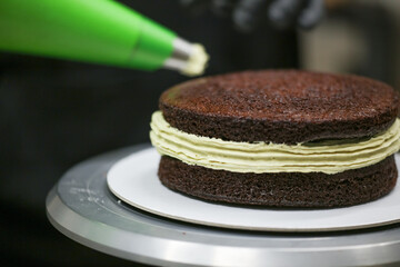pastry chef designer using pistachio cream filling piping bag on layered dark chocolate cake at kitchen lab