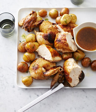 Faux-Tisserie Chicken cut into pieces with roasted potatoes on platter with gravy, studio shot