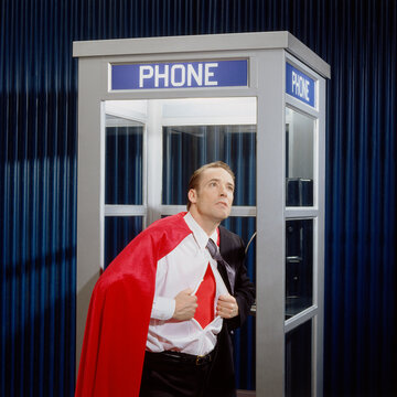 Man Opening Shirt to Reveal Super Hero Costume in Phone Booth