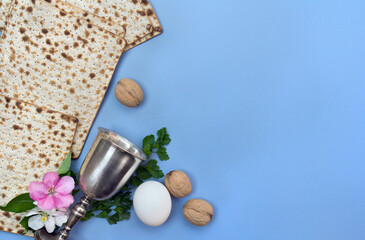 Matzo, wine, and pink flowers apple tree, nuts for passover celebration on blue table background with space for text. Top view, flat lay