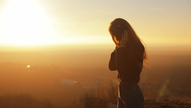 young woman listening to music in headphones at sunset. the wind blows the hair, against the background of a beautiful landscape and a yellow sky
