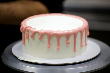 pastry chef making a pink dripping frosted cake for baby girl birthday celebration at kitchen lab
