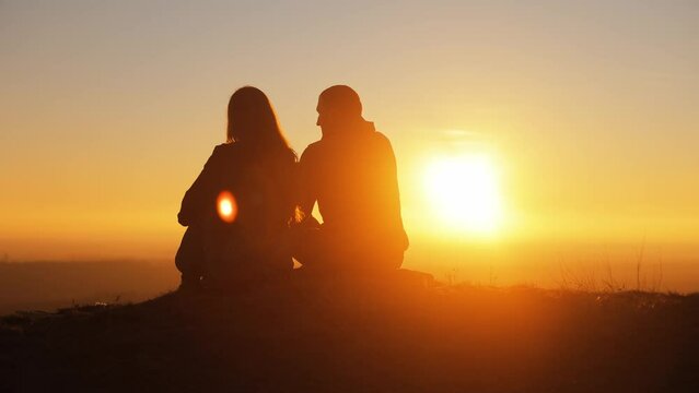 Silhouette of a couple against the sunset on top of a mountain. A man and a woman are sitting next to each other, admiring the sunset and the incredible landscape, spending time together, a date