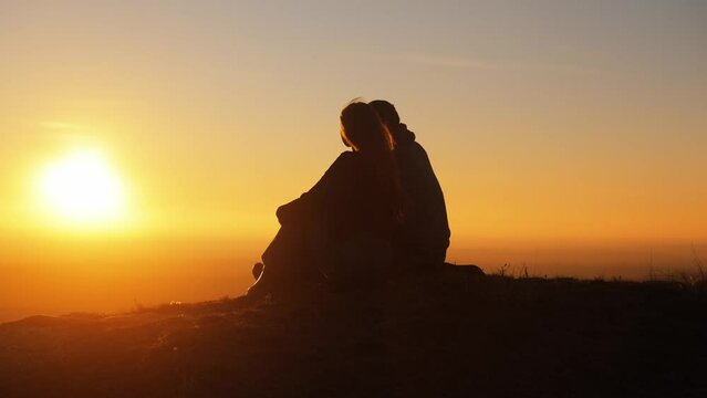 Silhouette of a couple against the sunset on top of a mountain. A man and a woman are sitting next to each other, admiring the sunset and the incredible landscape. Romance on Valentine's Day