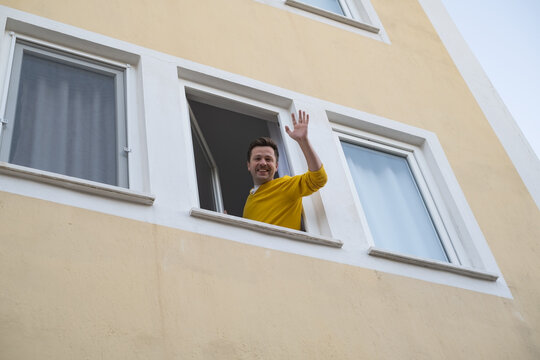 Mature man waving hand greeting his friend from window.