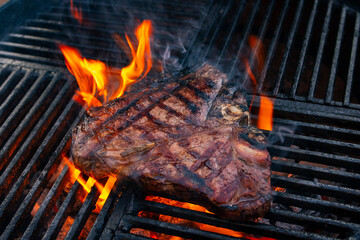 Barbecue dry aged wagyu porterhouse beef steak grilled as close-up on a charcoal grill with fire...
