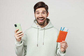 Traveler fun excited man wear hoody hold passport ticket use mobile cell phone isolated on plain solid white background. Tourist travel abroad in free spare time rest getaway. Air flight trip concept.