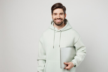 Young smiling programmer happy fun caucasian man wearing mint hoody hold use work on laptop pc...