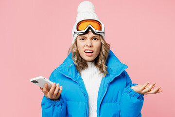 Snowboarder sad woman wear blue suit goggles mask hat ski padded jacket hold use mobile cell phone spread hands isolated on plain pastel pink background. Winter extreme sport hobby trip relax concept. © ViDi Studio