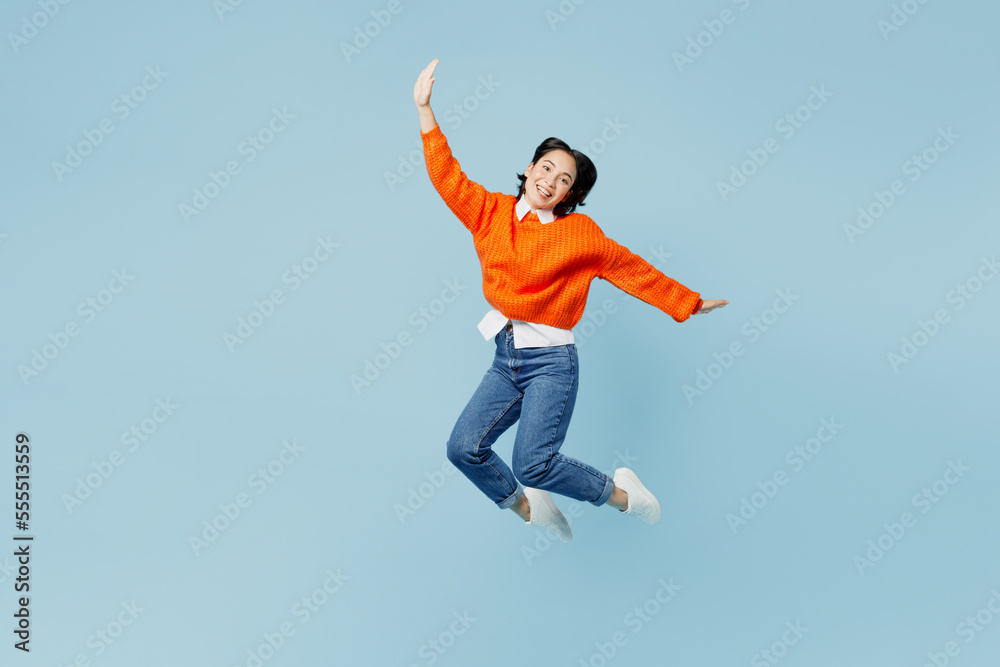 Wall mural full body fun young woman of asian ethnicity wear orange sweater glasses jump high with outstretched