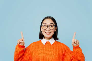Young smiling fun woman of Asian ethnicity wearing orange sweater glasses point index finger...