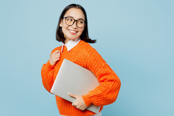 Side view young smiling fun smart IT woman of Asian ethnicity wear orange sweater glasses hold...