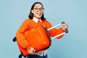 Side view traveler woman of Asian ethnicity wear orange sweater hold valise isolated on plain...