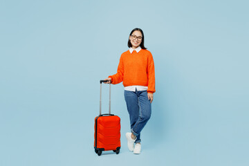 Full body traveler woman of Asian ethnicity wear orange sweater hold valise isolated on plain...
