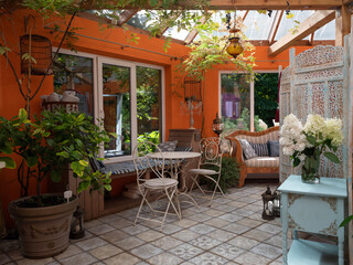 Fototapeta na wymiar Interior of veranda. Cozy space in patio. A lot of plants. Orange wall. Wooden vintage furniture.