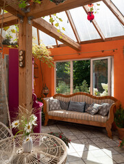 Interior of veranda. Cozy space in patio. A lot of plants. Orange wall. Wooden vintage furniture. Sofa with cushions.