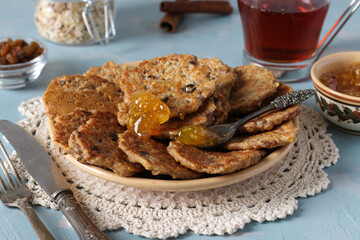 Oatmeal fritters with raisins are sprinkled with sweet syrup and served for breakfast with cup of tea