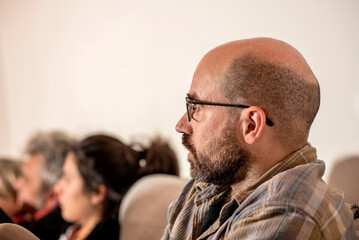 profile portrait of man with glasses and bald, attractive, watching TV with family on sofa, worried face