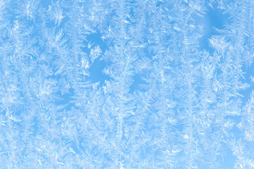Blue background. Beautiful pattern of frost on the window against the blue sky.