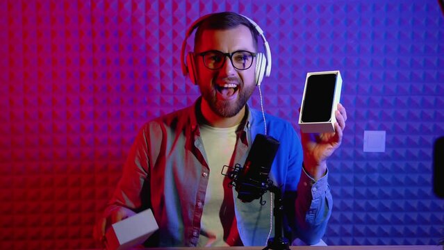 Excited overjoyed young male blogger unpacking boxe with new smartphone and doing live streaming. Attractive man using smart phone camera for creating content